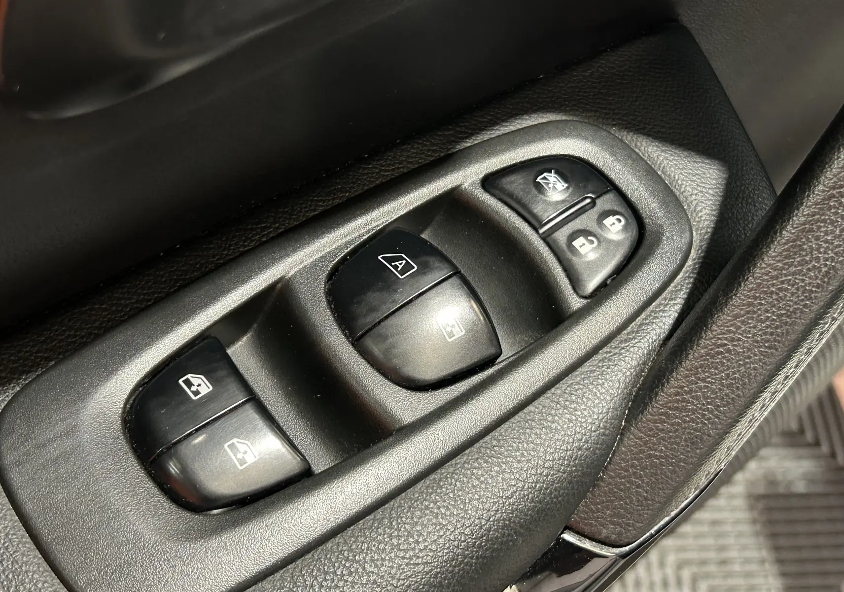 Gros plan sur les commandes de lève-vitres et verrouillage sur la porte côté conducteur d’un Renault Kadjar blanc.