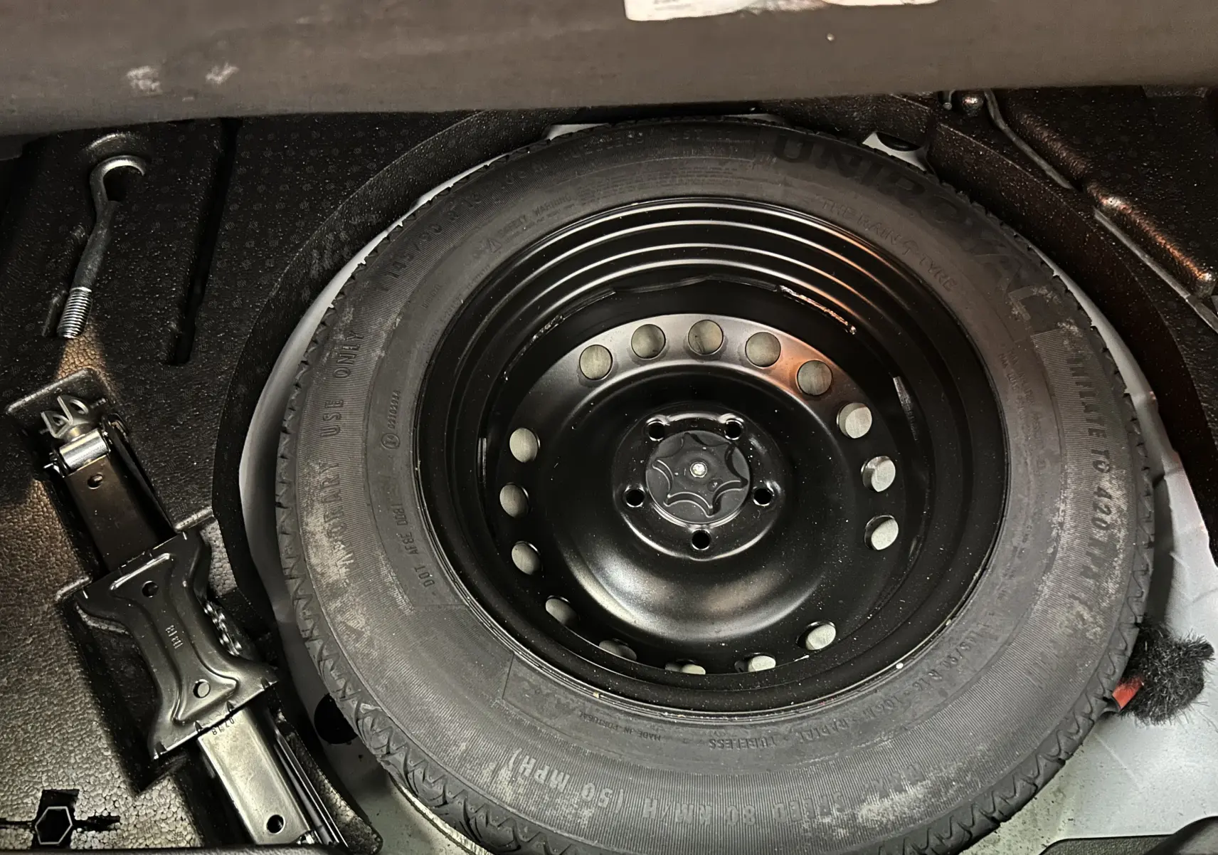 Gros plan sur la roue de secours noire et le cric dans le coffre d’un Renault Kadjar blanc de 2018.