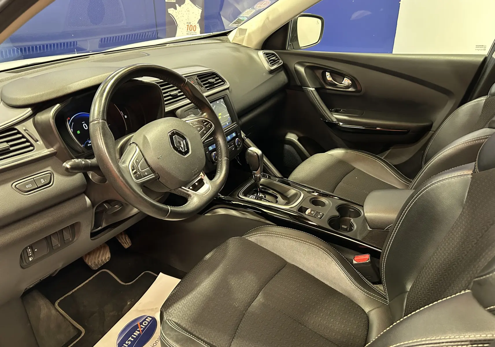 Vue intérieure côté conducteur du Renault Kadjar blanc 2018, avec volant cuir et console centrale brillante.