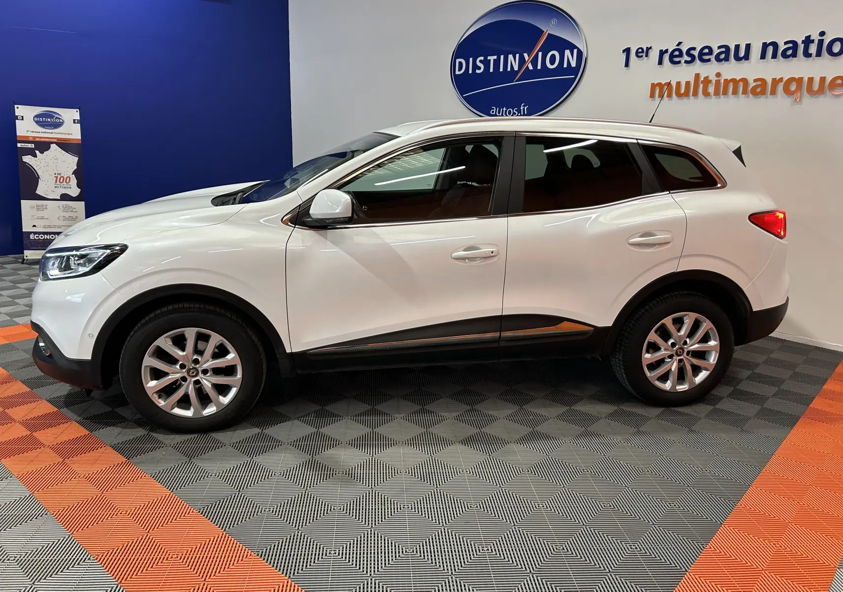 Vue latérale droite d'un Renault Kadjar blanc 2018 en showroom, avec jantes alliage et attelage visible à l'arrière.