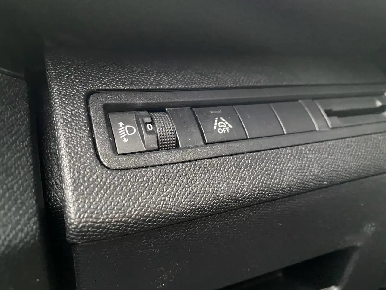 Gros plan sur les commandes de réglage des phares et d'aide à la conduite du tableau de bord d'un Peugeot 3008 gris platinium.