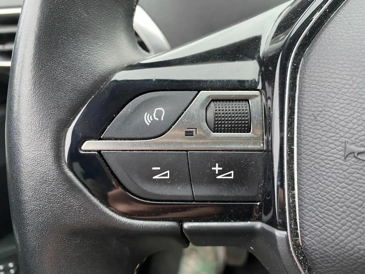 Gros plan sur les commandes de volume et de fonction vocale du volant noir du Peugeot 3008 gris platinium 2021.