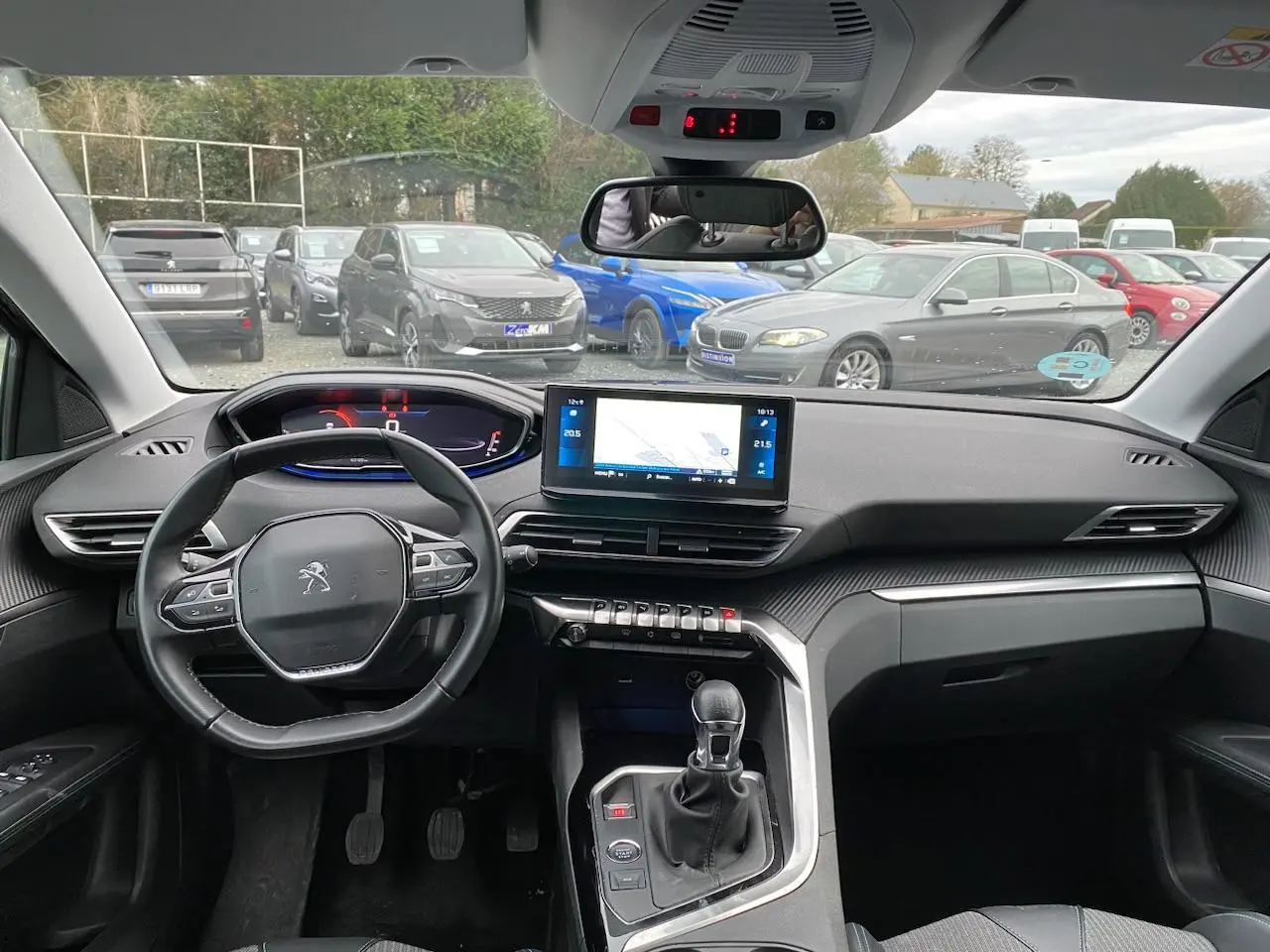 Vue intérieure avant du Peugeot 3008 gris platinium 2021, volant compact, écran tactile GPS et boîte manuelle visible.