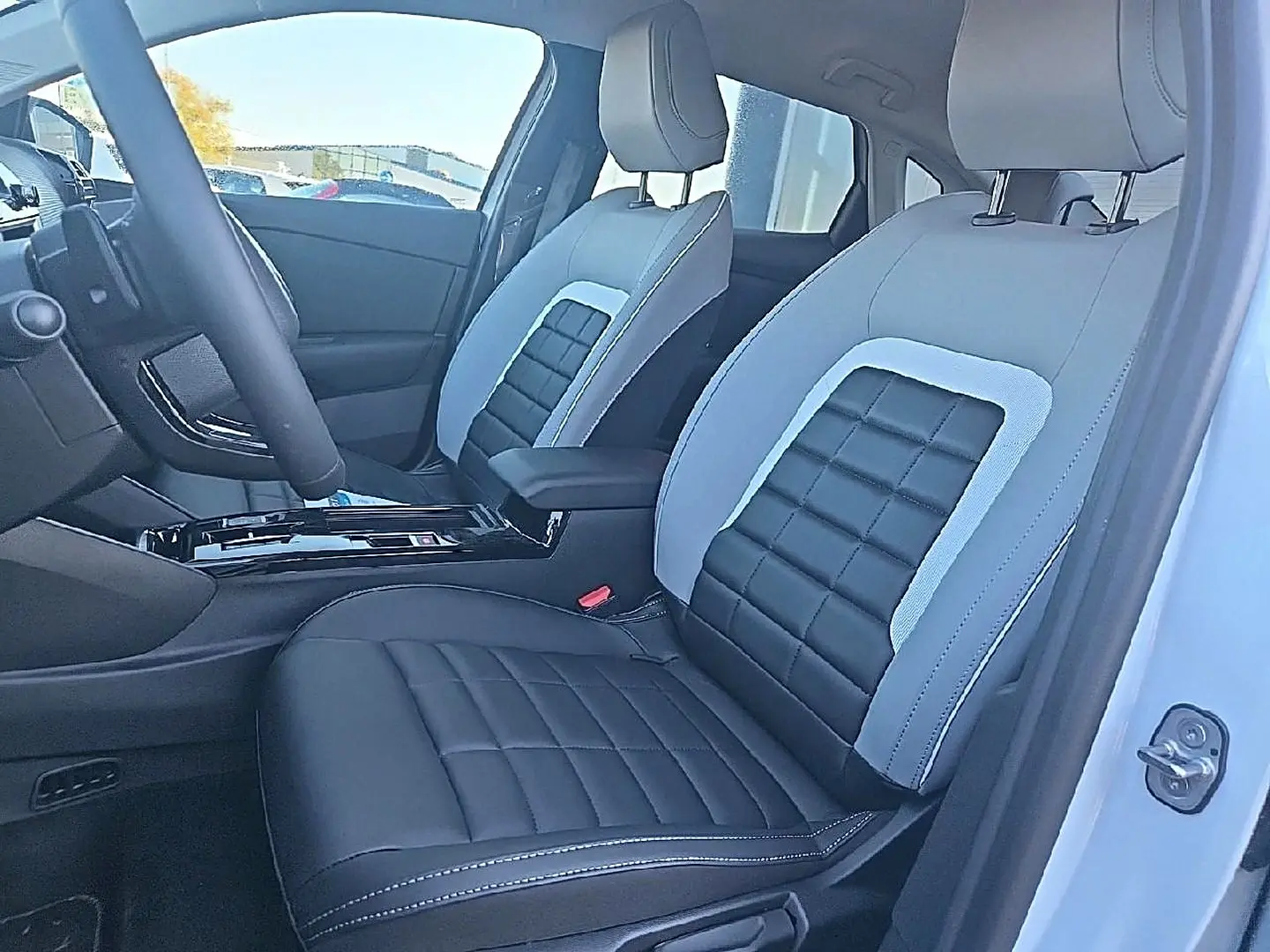 Vue intérieure côté conducteur de la Citroën C4 X blanche, sièges bi-ton noir et gris avec accoudoir central.