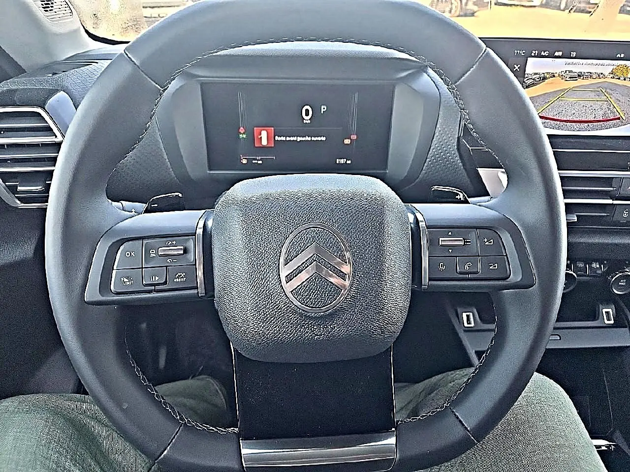 Vue centrée sur le volant cuir noir de la Citroën C4 X 1.2 hybride, avec tableau de bord numérique et écran de caméra de recul.