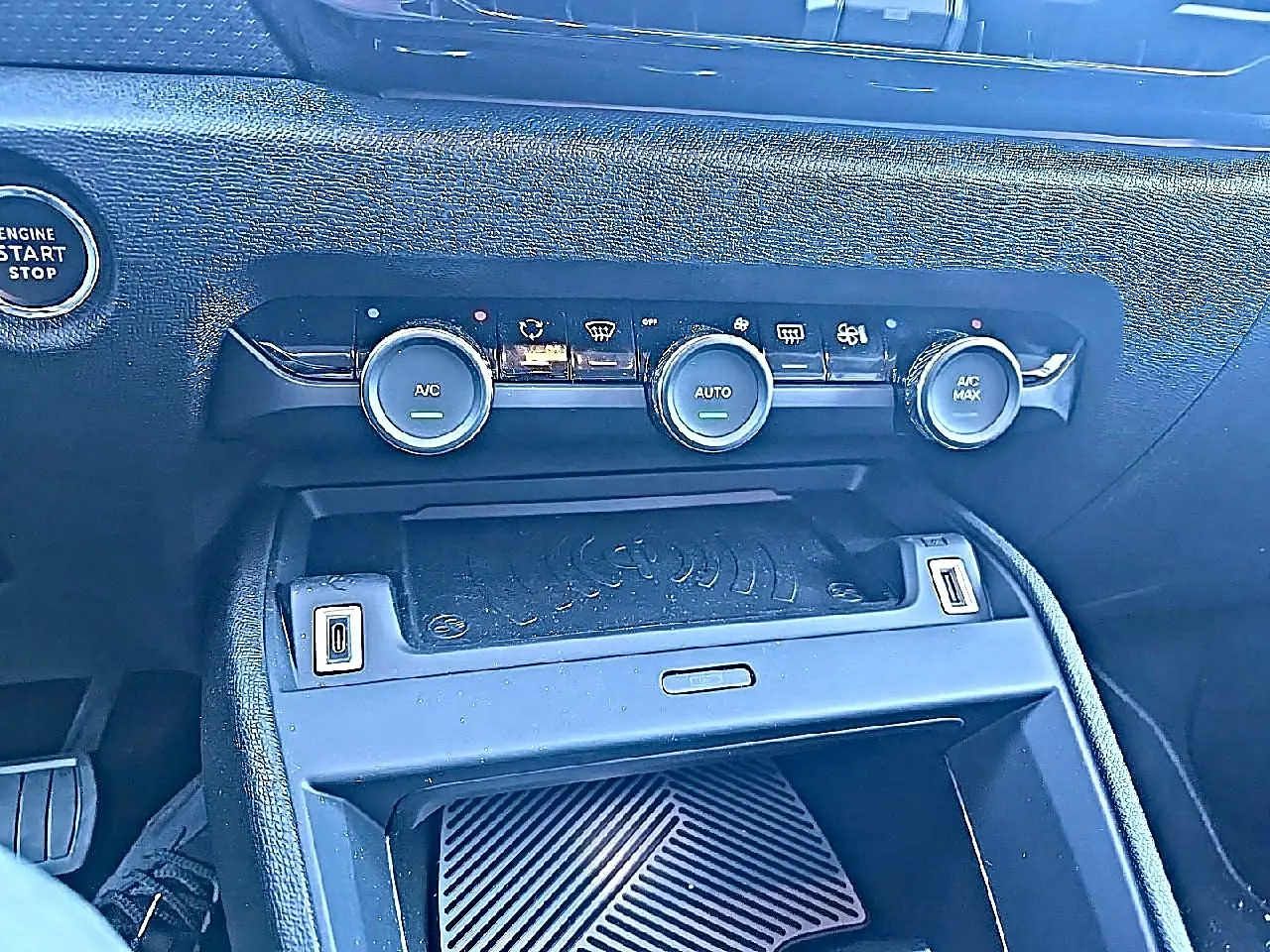 Vue rapprochée de la console centrale noire du Citroën C4 X 1.2 hybride, montrant les commandes de climatisation et prises USB.