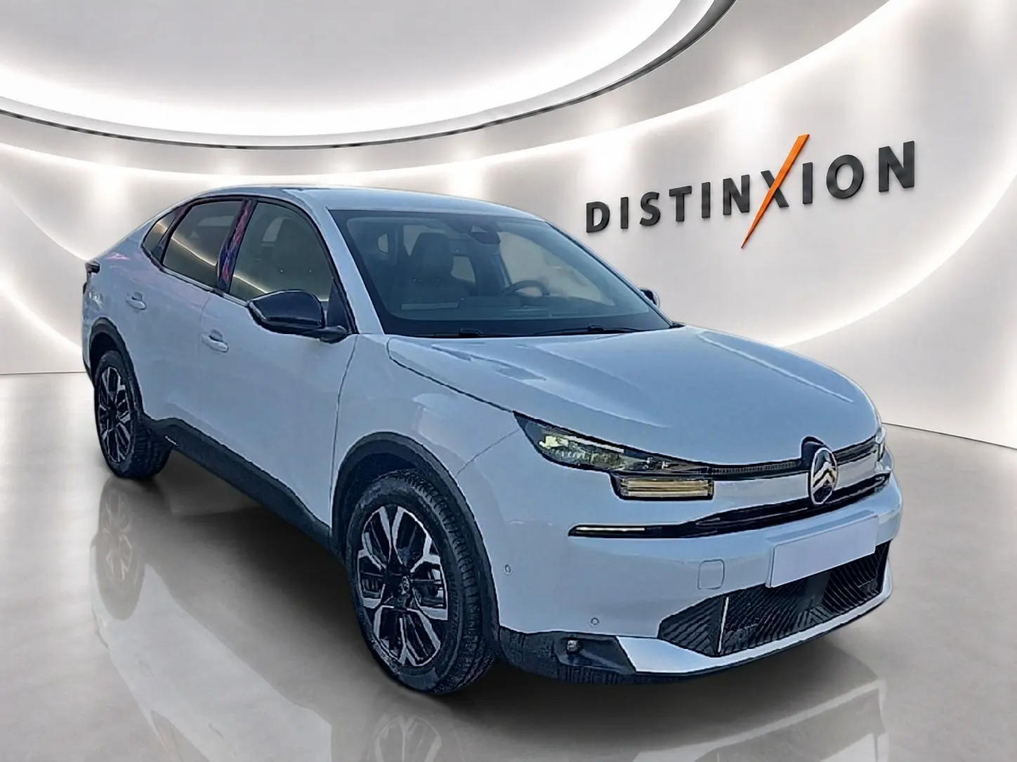 Vue 3/4 avant d'une Citroën C4 X blanche avec jantes alu noires, dans un showroom lumineux au logo Distinxion.