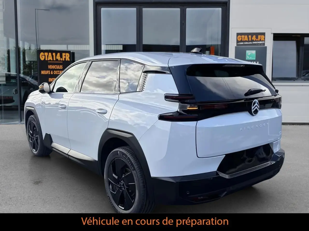 Vue 3/4 arrière droite d’un Citroën C5 Aircross hybride blanc avec toit noir et jantes noires devant un bâtiment.