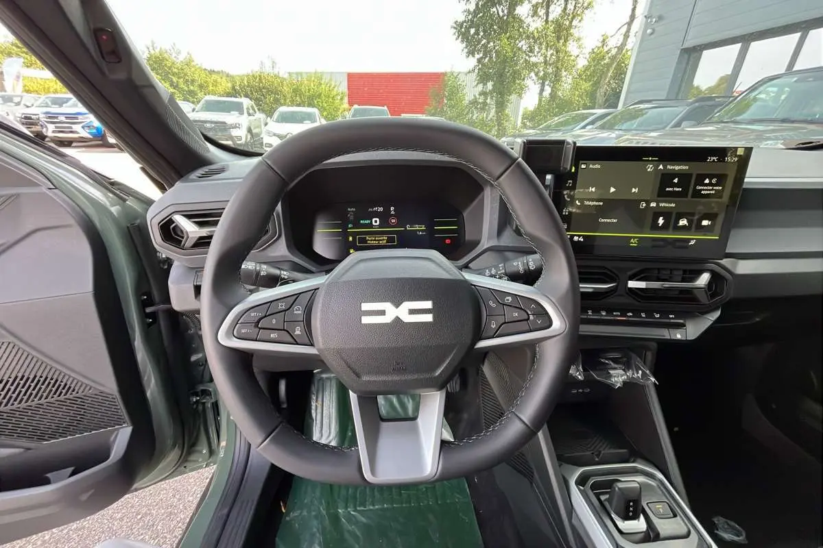 Vue intérieure centrée sur le volant et tableau de bord du Dacia Duster Hybrid-G 150 4x4 en kaki lichen, avec écran tactile.
