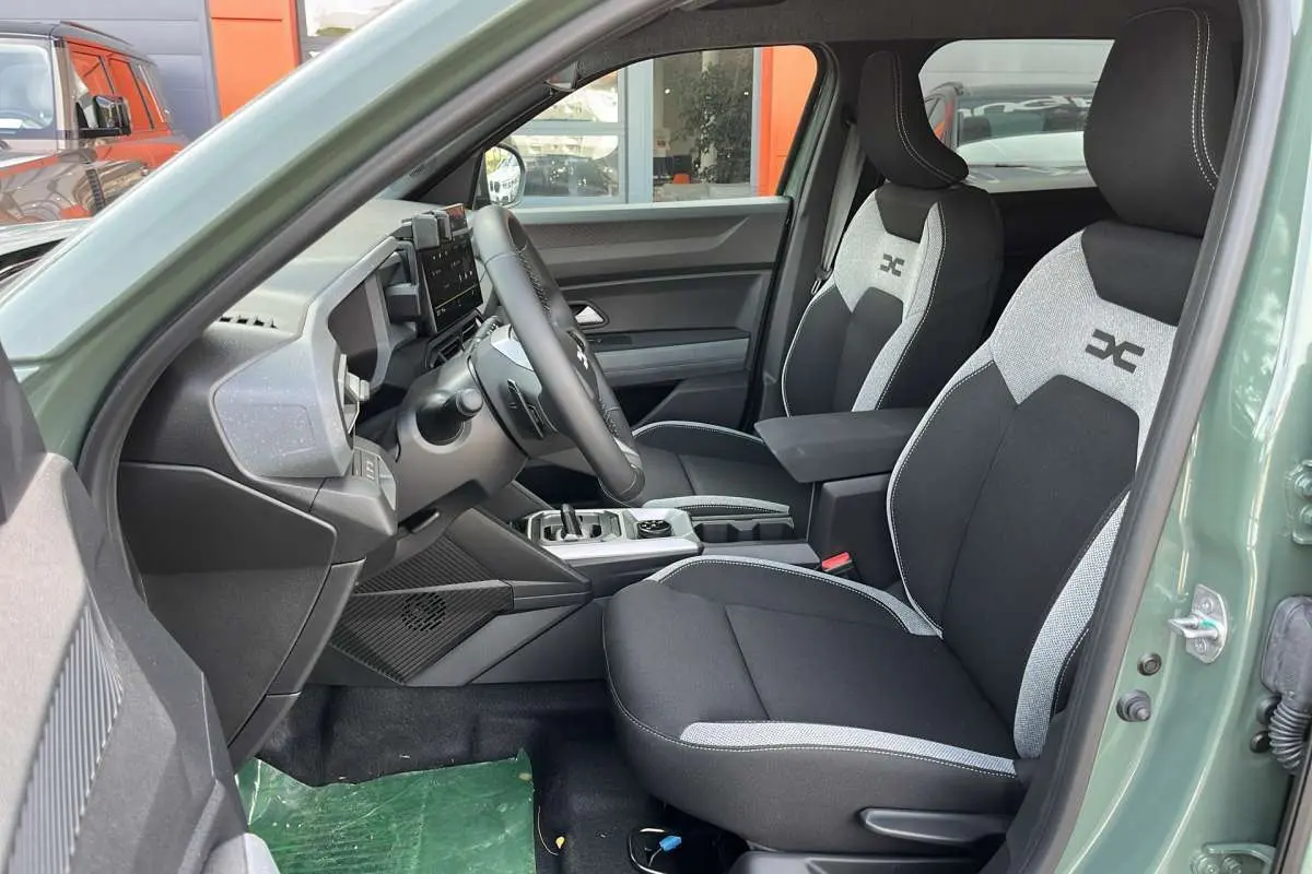 Vue intérieure côté conducteur du Dacia Duster 2026 kaki lichen, avec sièges bi-ton et accoudoir central avant.