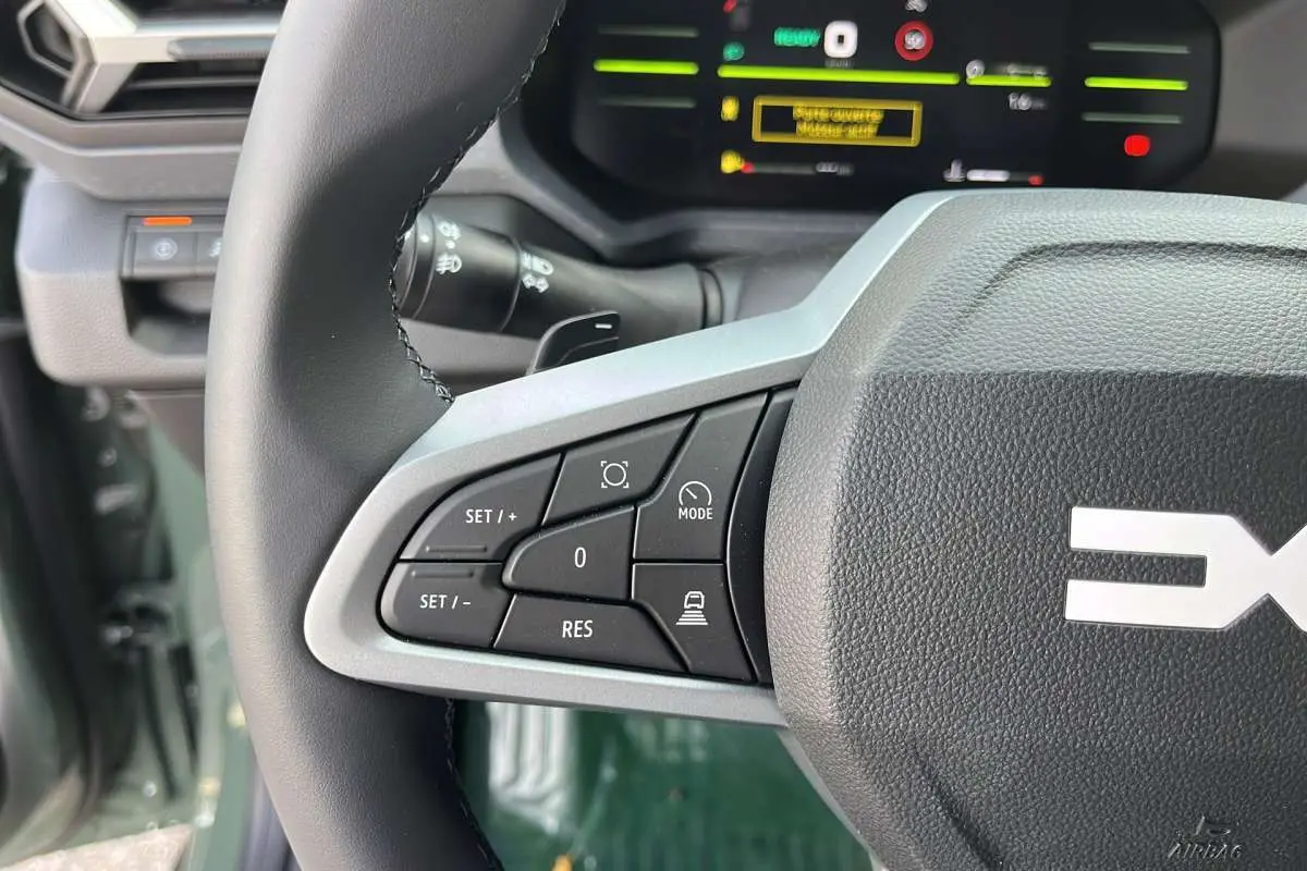 Gros plan sur le volant cuir du Dacia Duster Hybrid-G 150, montrant les commandes de régulateur et d'aide à la conduite.