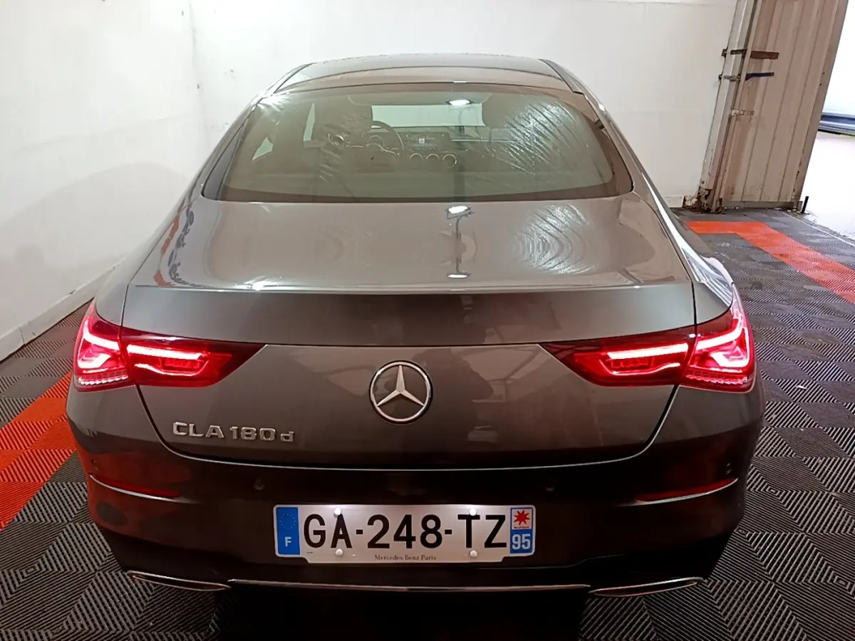 Vue arrière d'une Mercedes CLA 180 d gris clair avec feux LED allumés dans un garage fermé.