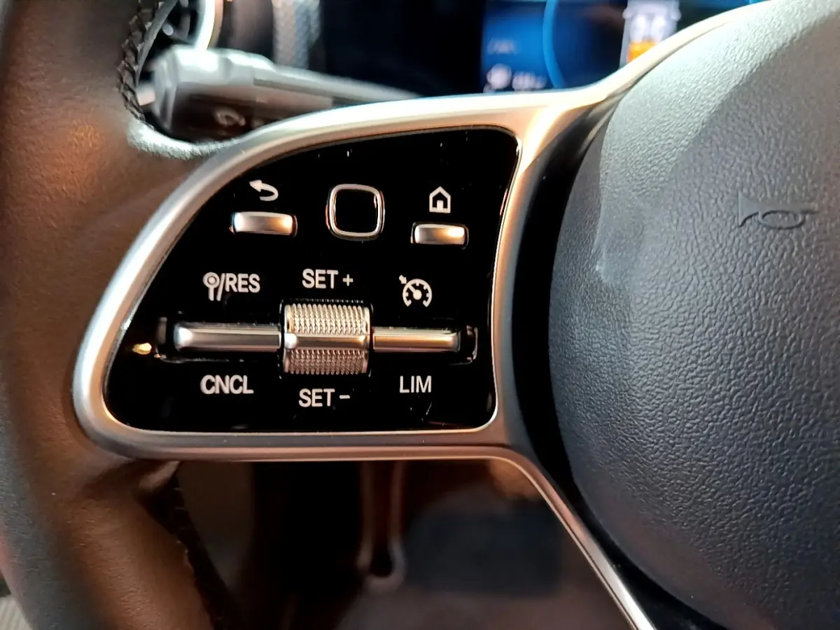 Gros plan sur les commandes de régulateur de vitesse à gauche du volant cuir noir d’une Mercedes CLA 180 d Business Line 2021.