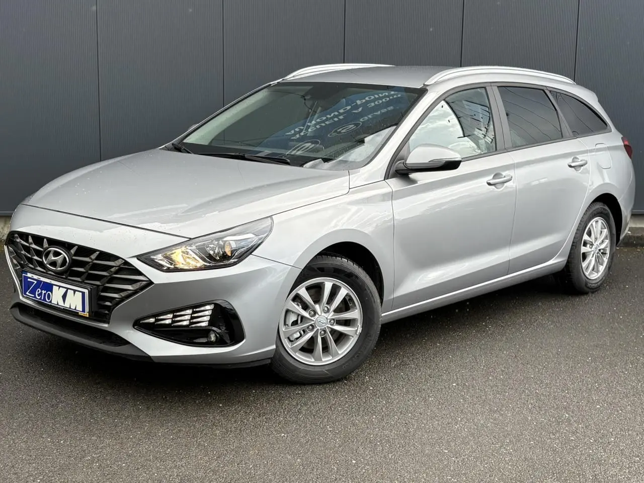 Hyundai i30 SW gris argent vue 3/4 avant droit, avec jantes alliage et projecteurs allumés.