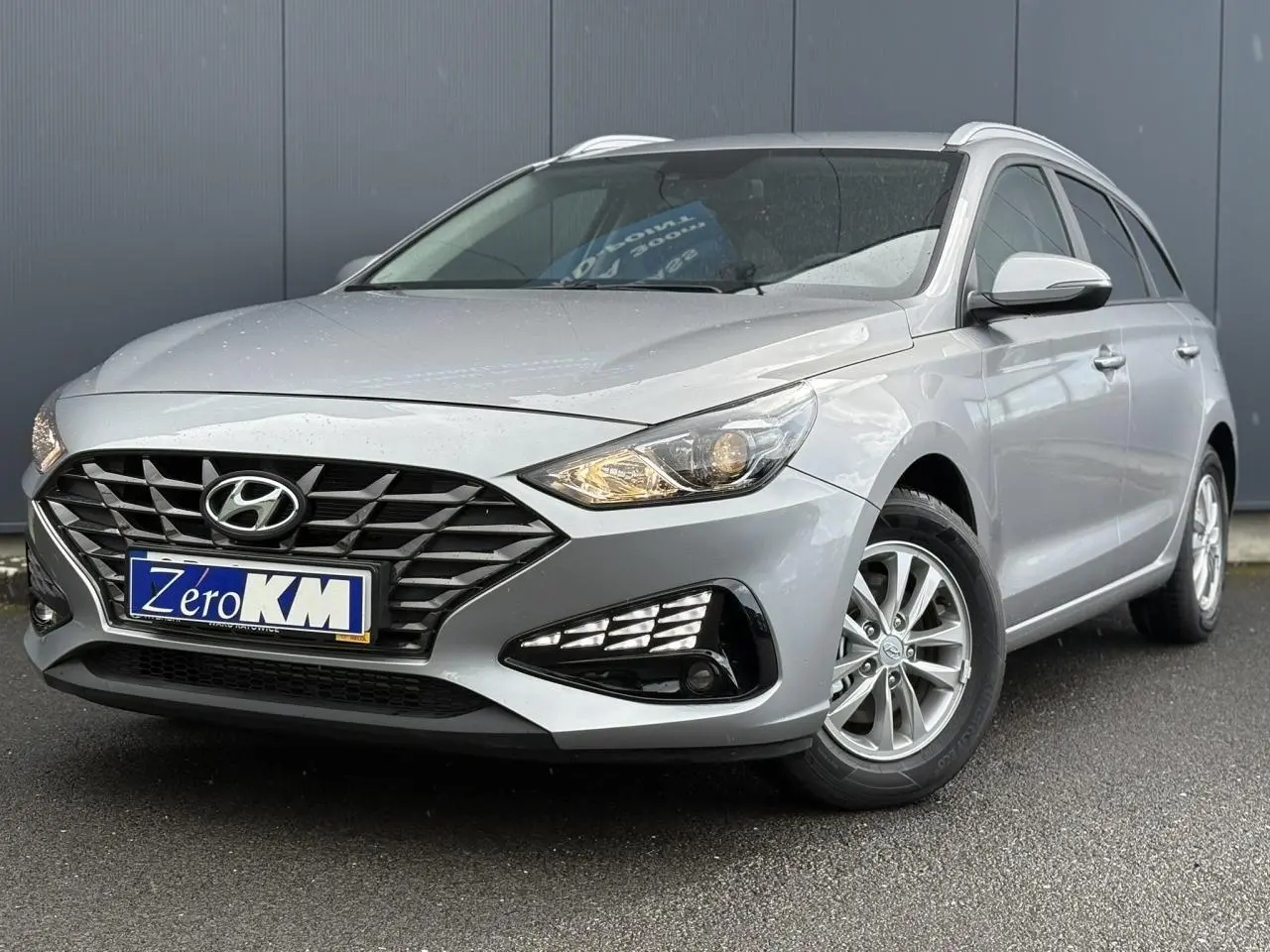 Hyundai i30 SW gris argent vue 3/4 avant droit, avec calandre noire et jantes alliage visibles.