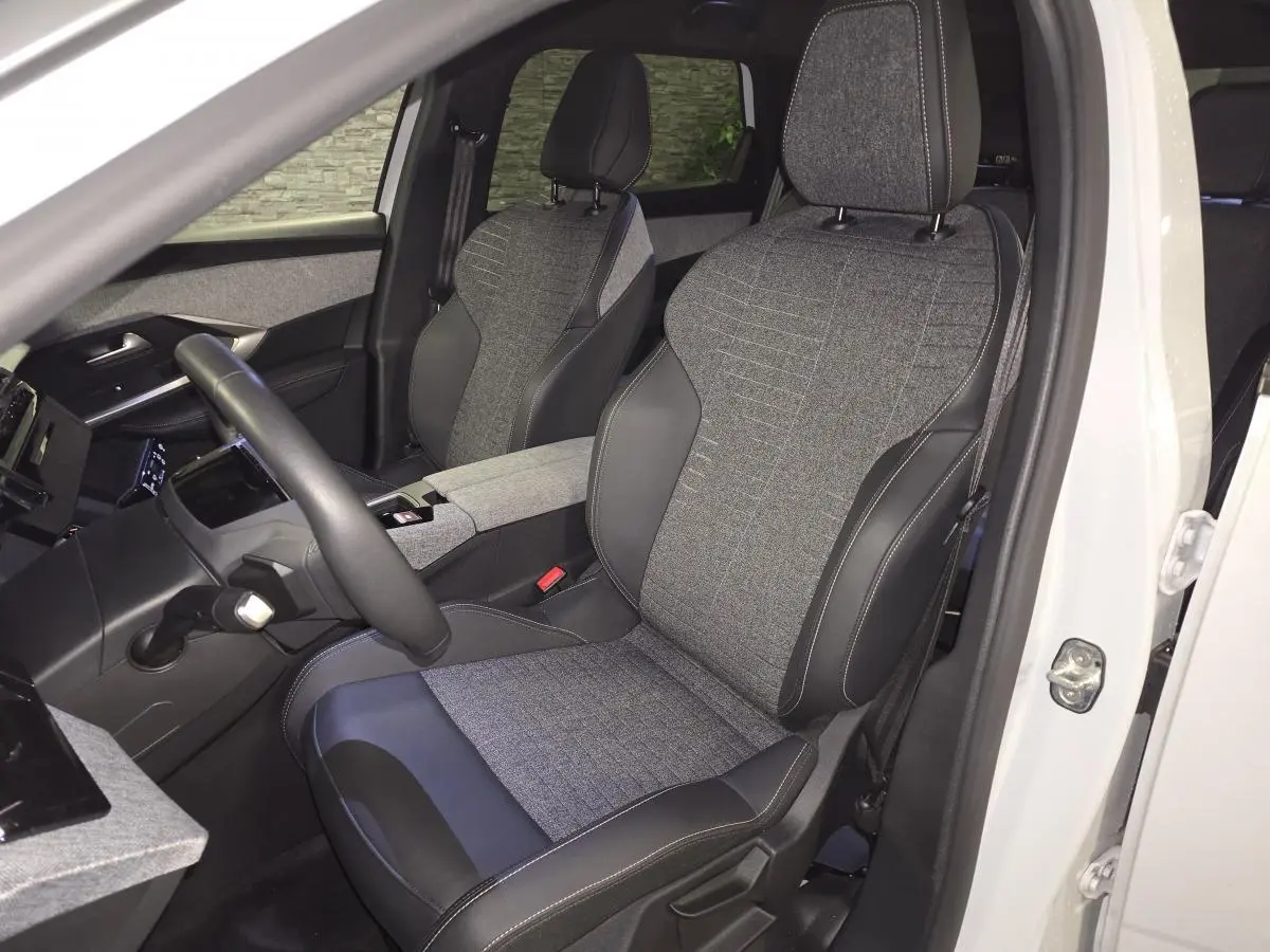 Vue intérieure côté conducteur du Peugeot 5008 blanc 2025, sièges tissu gris et cuir noir avec surpiqûres.