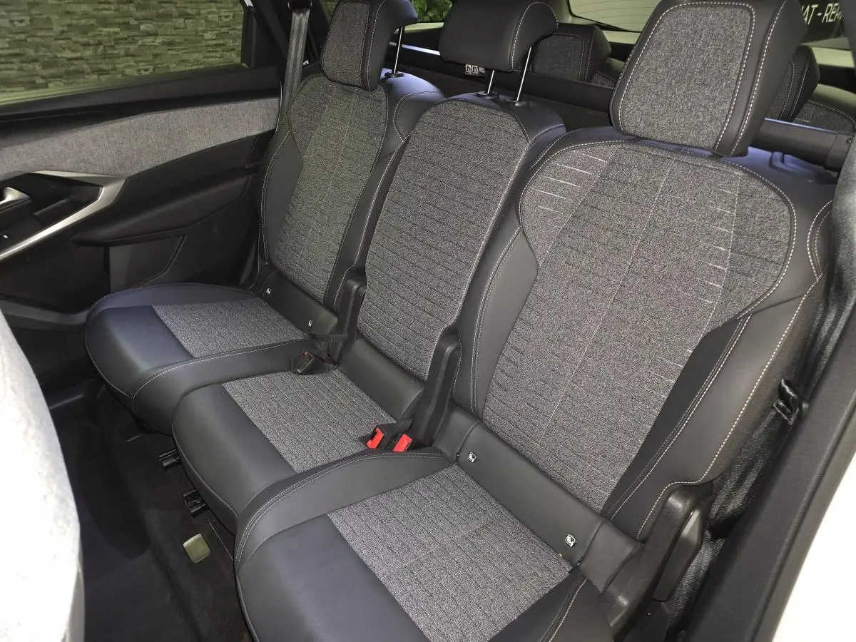 Vue intérieure sur la banquette arrière tissu gris et cuir noir du Peugeot 5008 blanc 2025, avec ceintures et appuie-têtes.