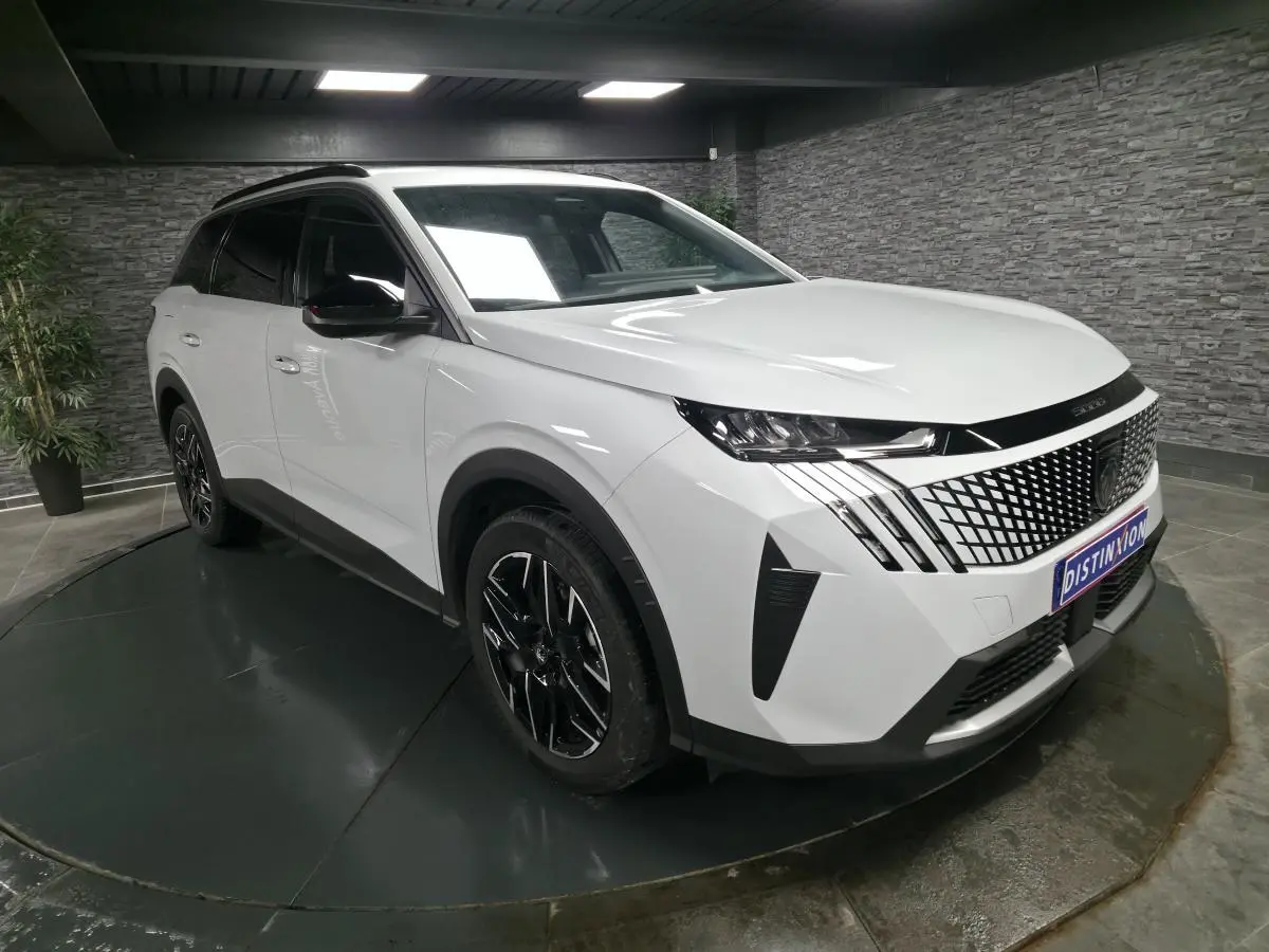 Peugeot 5008 blanc vue 3/4 avant droit avec calandre noire à motif géométrique et jantes alliage noires.