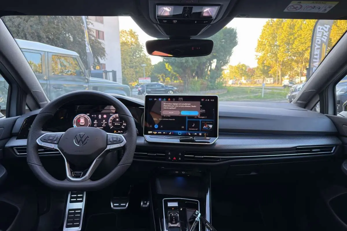 Vue intérieure avant de la Volkswagen Golf gris argent avec volant multifonctions et écran tactile central allumé.