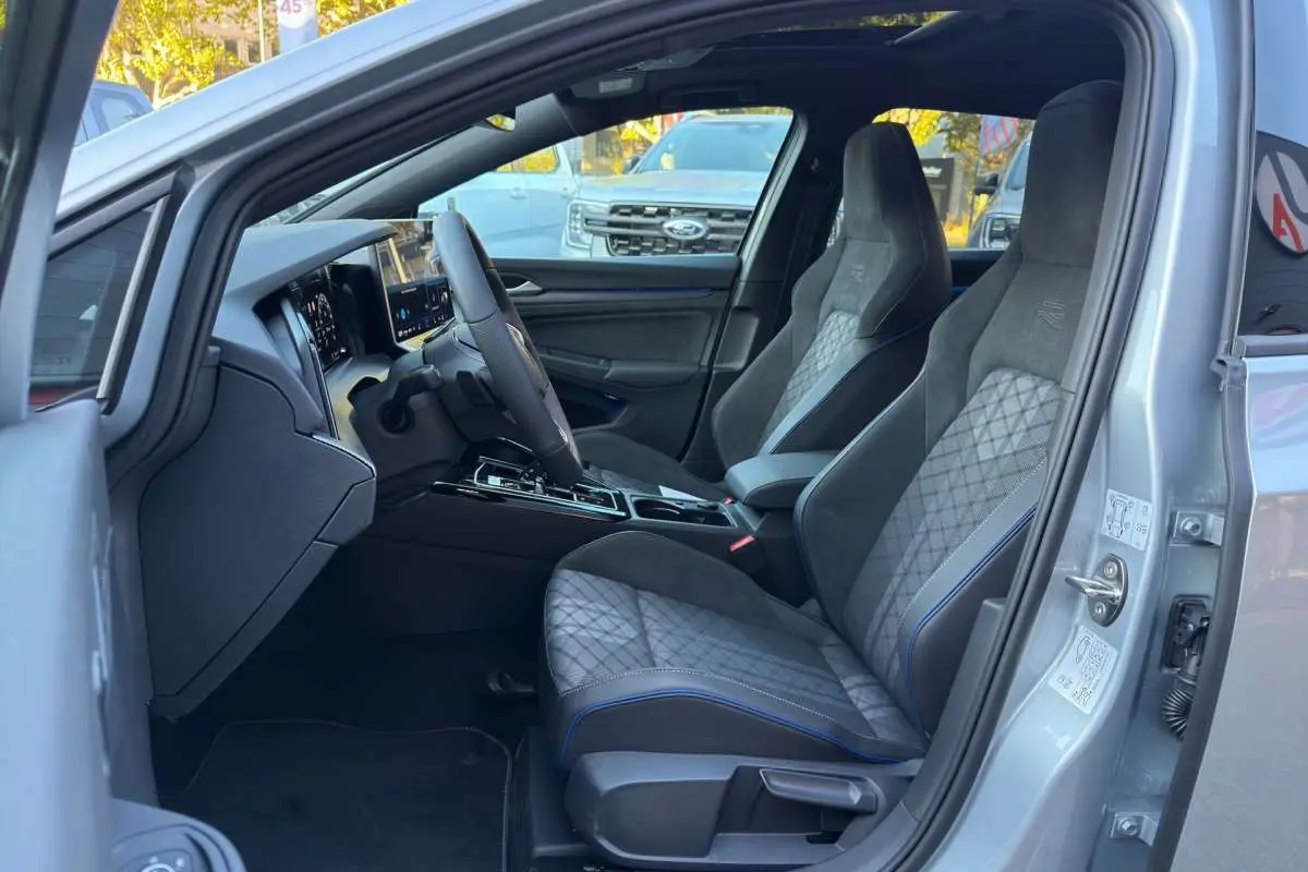 Intérieur de la Volkswagen Golf E-TSI 150 R-Line 2026, vue côté conducteur, sièges sport gris avec surpiqûres bleues.