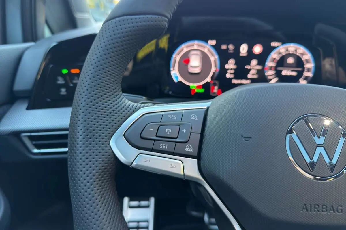 Gros plan sur le volant multifonctions en cuir de la Volkswagen Golf E-TSI, avec tableau de bord numérique en arrière-plan.