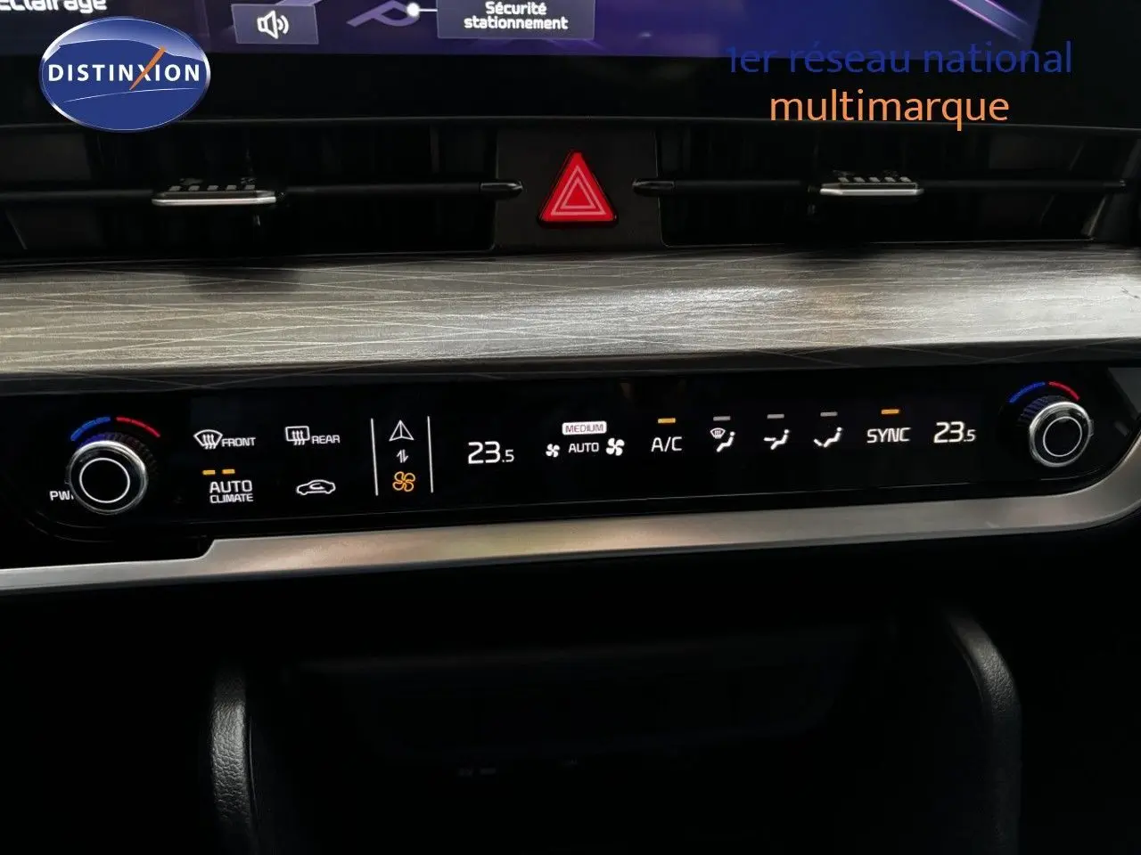 Tableau de bord du Kia Sportage blanc nacré, vue centrée sur la console de climatisation digitale avec finition bois clair.