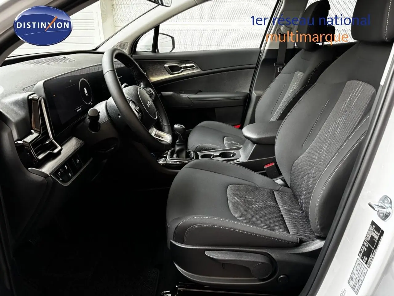 Vue intérieure côté conducteur du Kia Sportage blanc nacré, mettant en valeur les sièges noirs et la console centrale avec boîte manuelle.