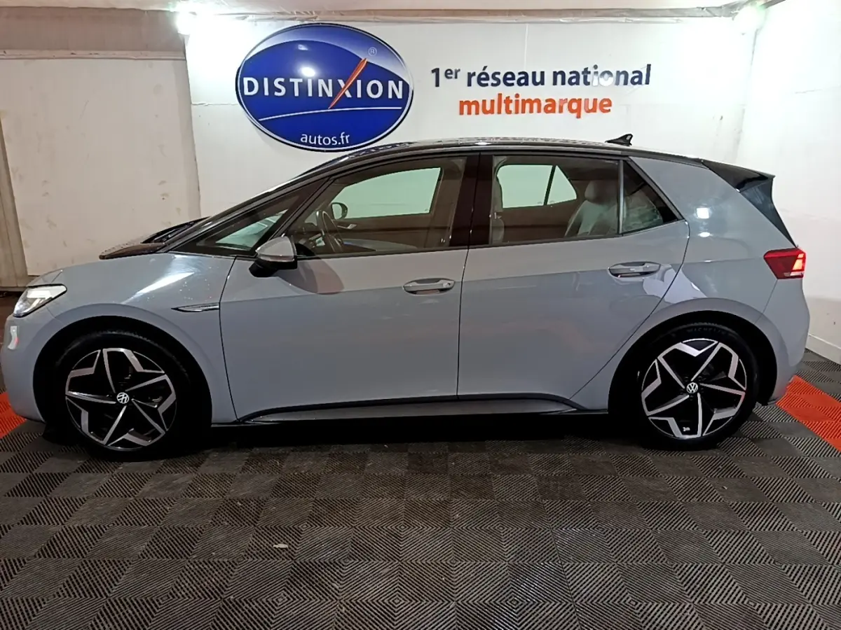Vue de profil côté gauche d'une Volkswagen ID.3 77 kWh Pro S gris foncé avec jantes noires et argentées, en intérieur showroom.