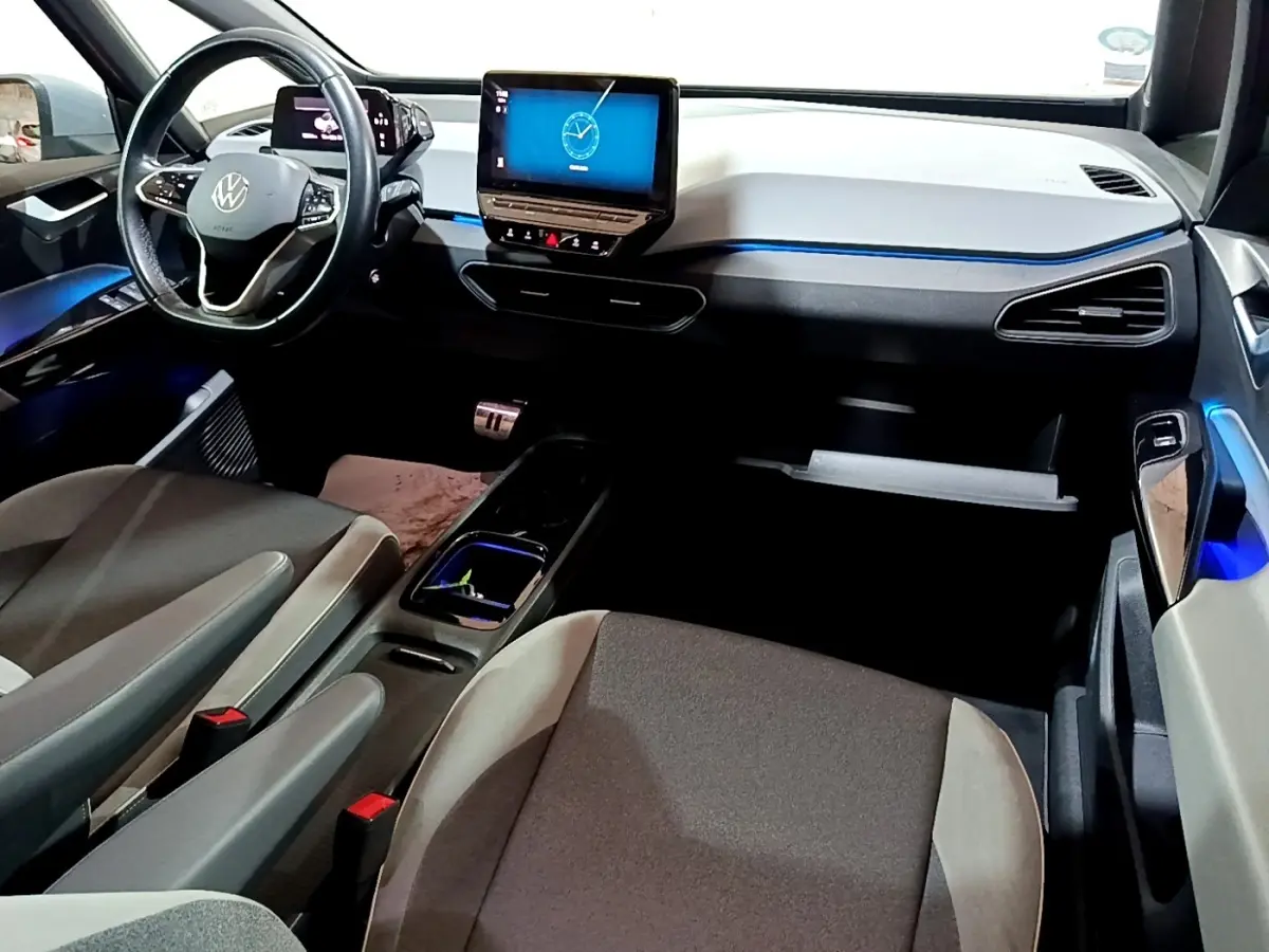 Vue intérieure avant du Volkswagen ID.3 77 kWh Pro S, tableau de bord clair avec écran tactile central et éclairage d'ambiance bleu.
