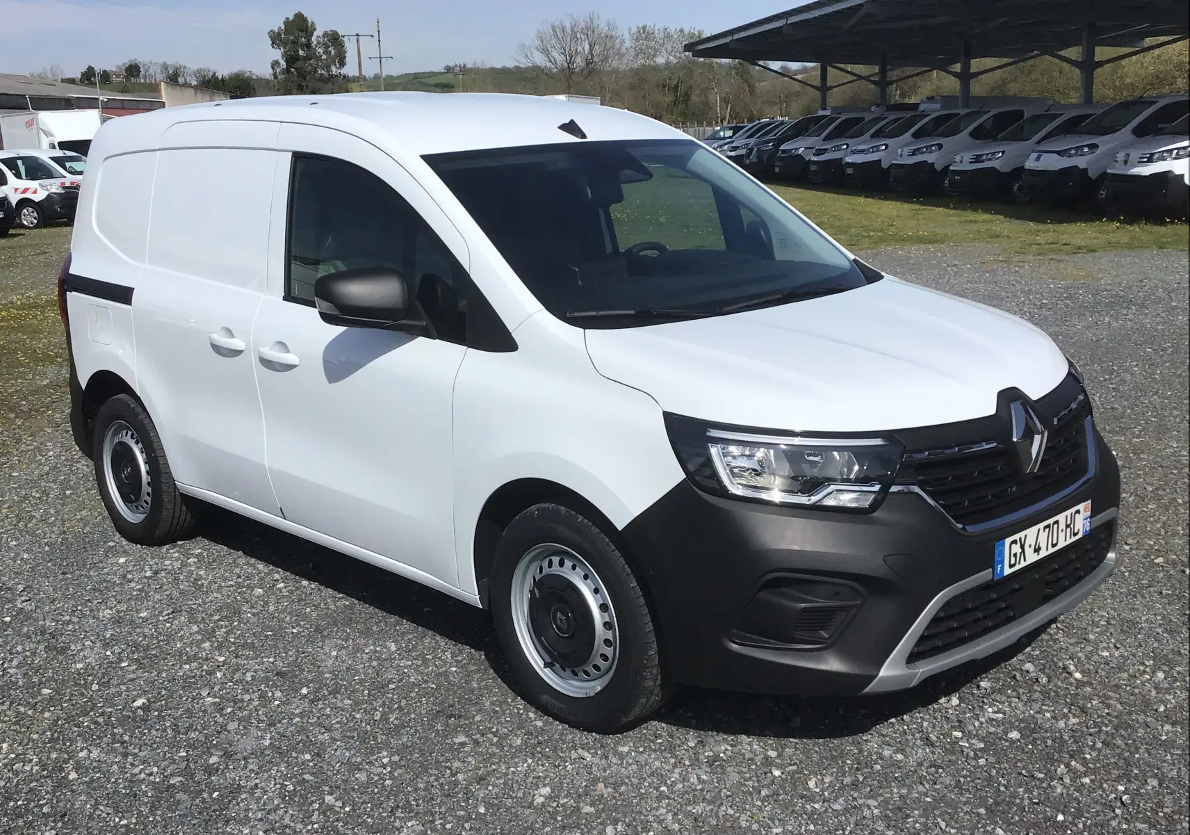 Vue 3/4 avant droit d’un Renault Kangoo Van blanc 2024 avec pare-chocs noir et jantes tôles sur un parking.
