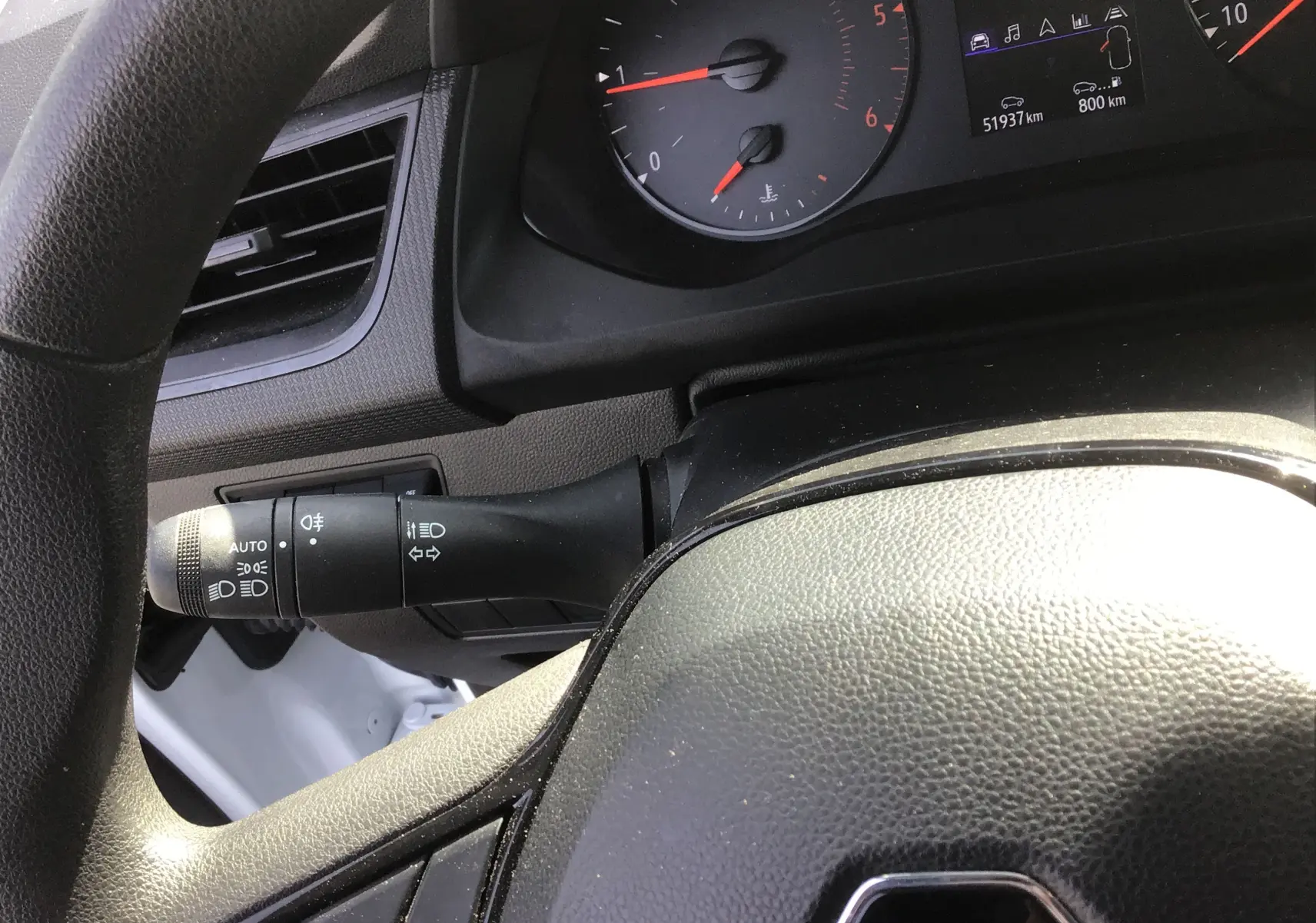 Gros plan sur le volant noir et le commodo gauche du tableau de bord du Renault Kangoo blanc 2024, avec compteurs visibles.