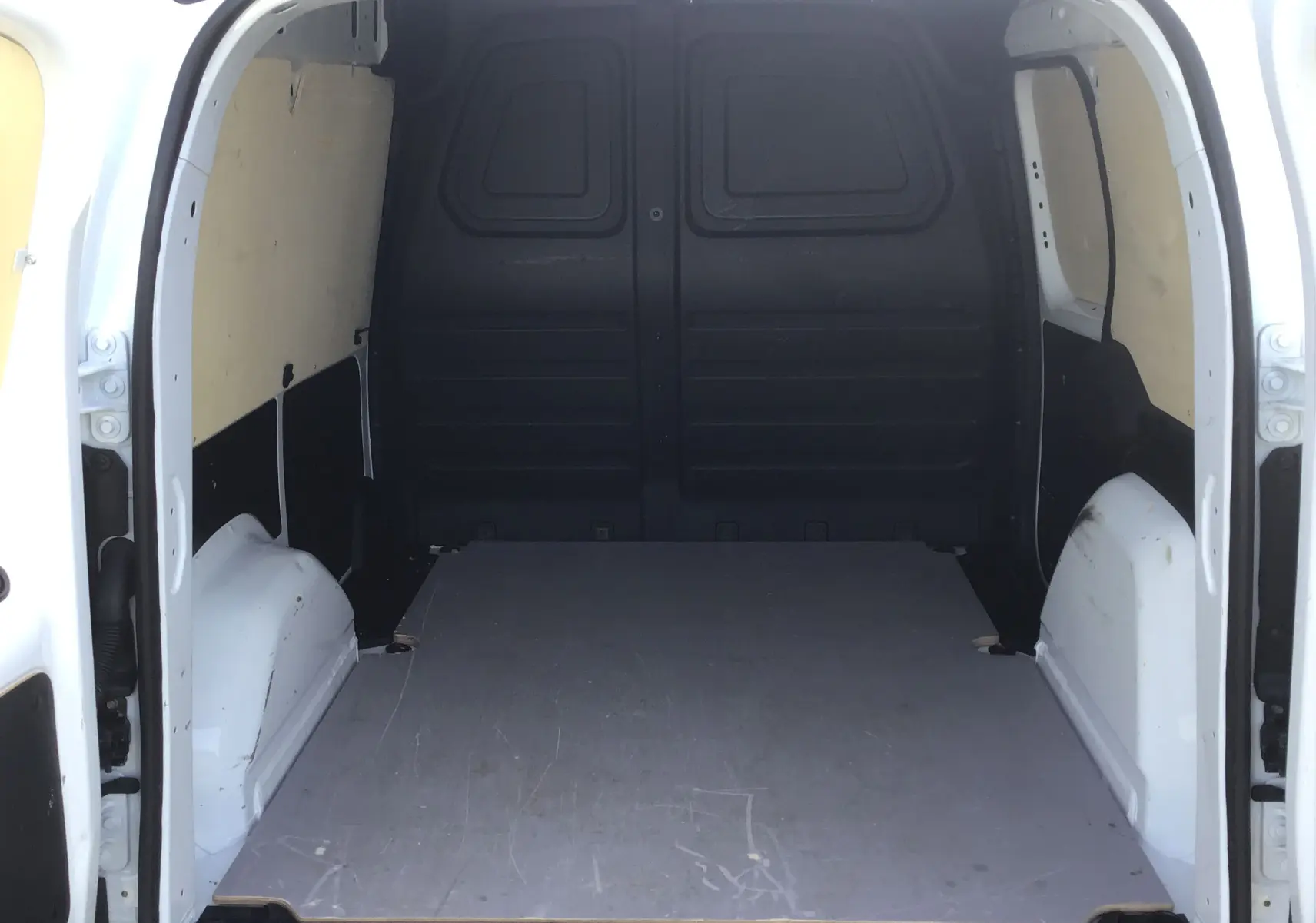 Vue intérieure arrière du Renault Kangoo Van blanc 2024, montrant l’espace de chargement vide avec parois latérales protégées.