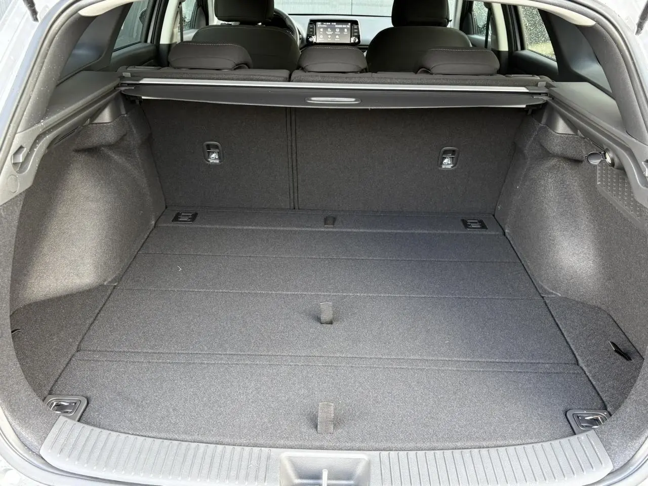 Coffre spacieux ouvert vu de l'arrière d'une Hyundai i30 SW gris argent, avec cache-bagages et sièges rabattus.