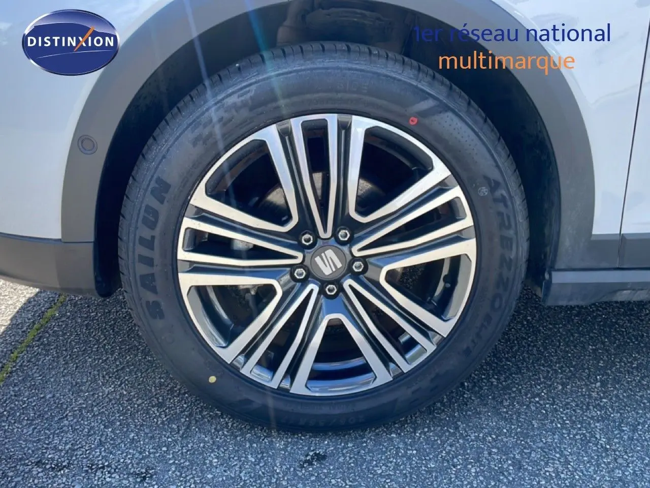 Gros plan sur la roue avant droite d’un SEAT Arona blanc avec jante alliage noire et argentée, partie de la carrosserie visible.