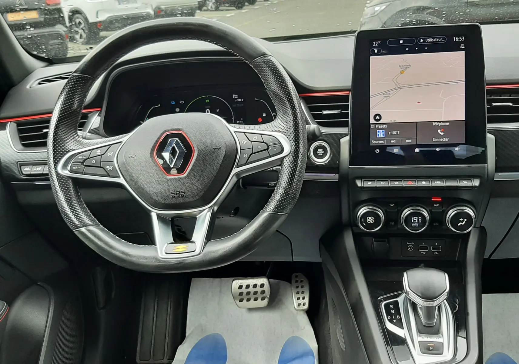 Vue intérieure centrée sur le volant et la console centrale d'une Renault Arkana E-Tech bleu Zanzibar avec écran tactile vertical.