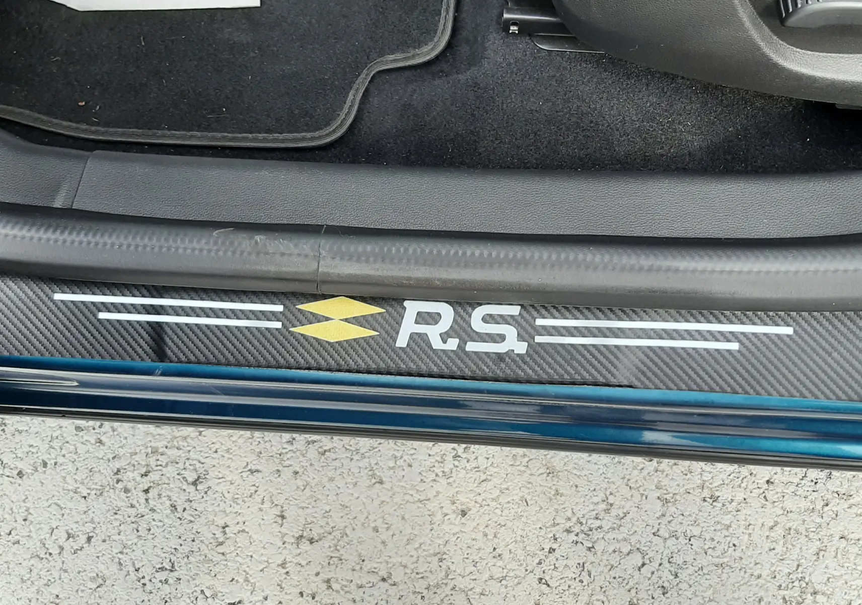 Vue rapprochée de la porte côté gauche du Renault Arkana Bleu Zanzibar, avec logo RS sur la plaque de seuil en carbone.