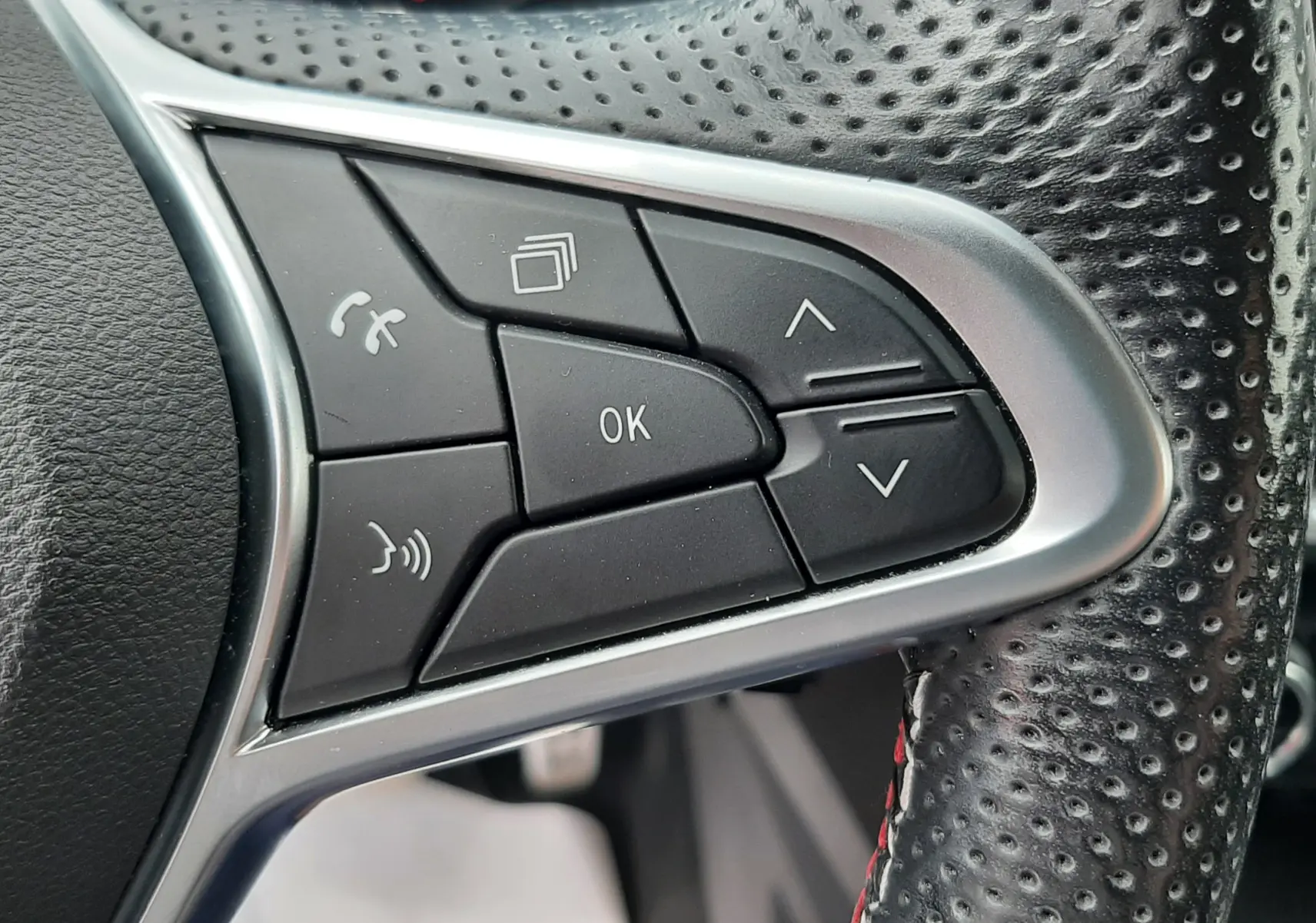 Gros plan sur les commandes noires et argentées au volant perforé d'une Renault Arkana E-Tech 145ch RS-Line.