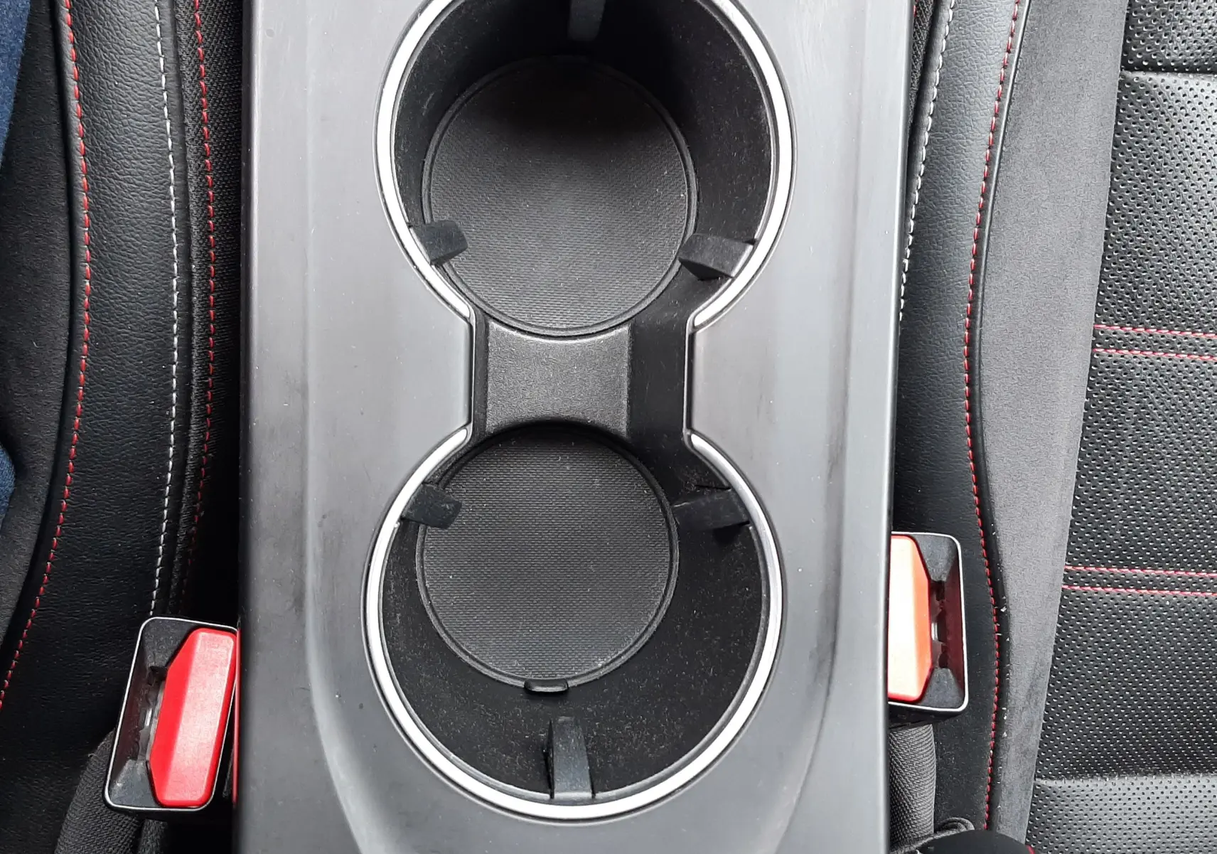 Vue plongeante sur la console centrale noire avec porte-gobelets et surpiqûres rouges des sièges du Renault Arkana E-Tech 145ch RS-Line.