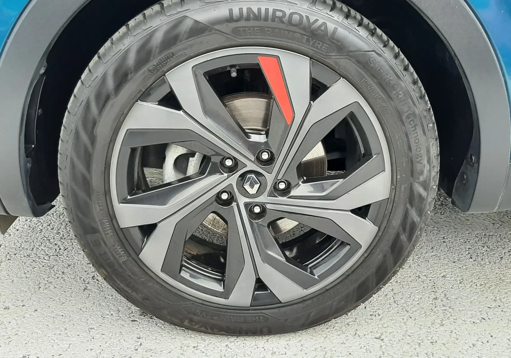 Gros plan sur la roue avant droite du Renault Arkana E-Tech bleu Zanzibar, avec jante noire et détail rouge distinctif.