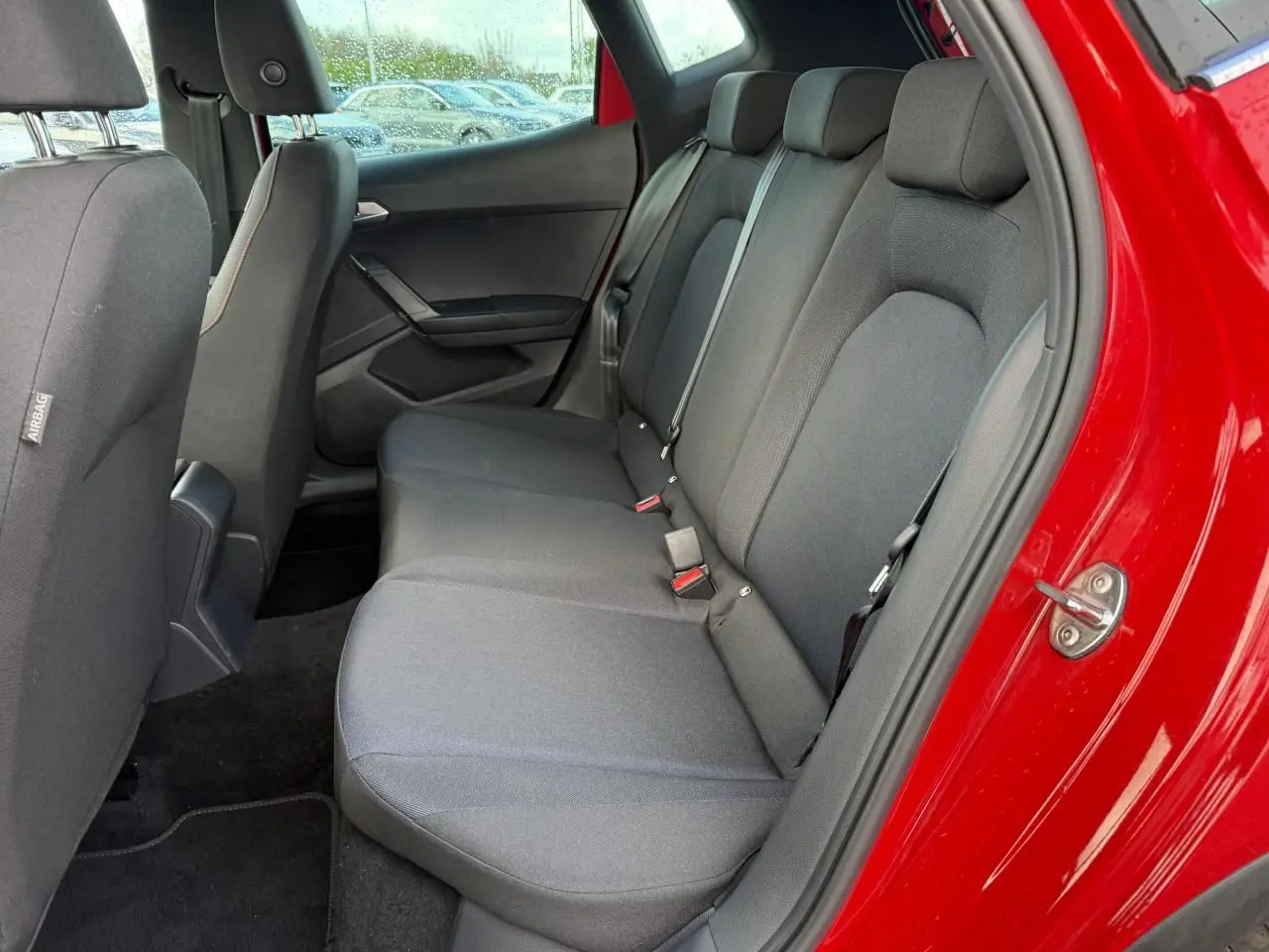 Vue intérieure côté arrière droit du SEAT Arona rouge 2024, montrant la banquette arrière en tissu gris foncé.