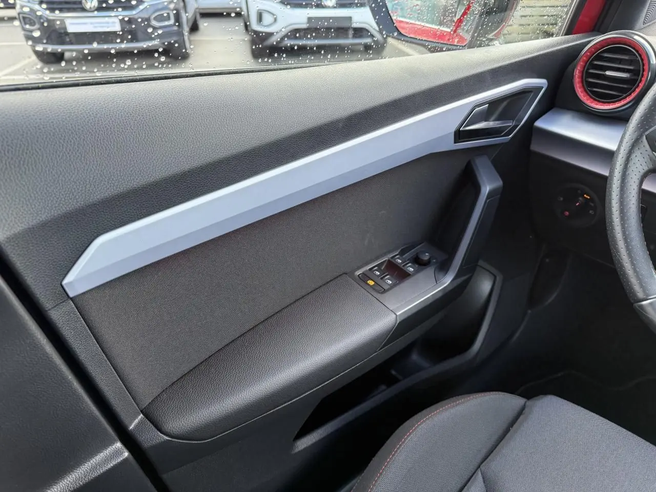 Vue intérieure côté gauche de la porte avant d'un SEAT Arona 2024 avec commandes électriques et habillage noir et gris.