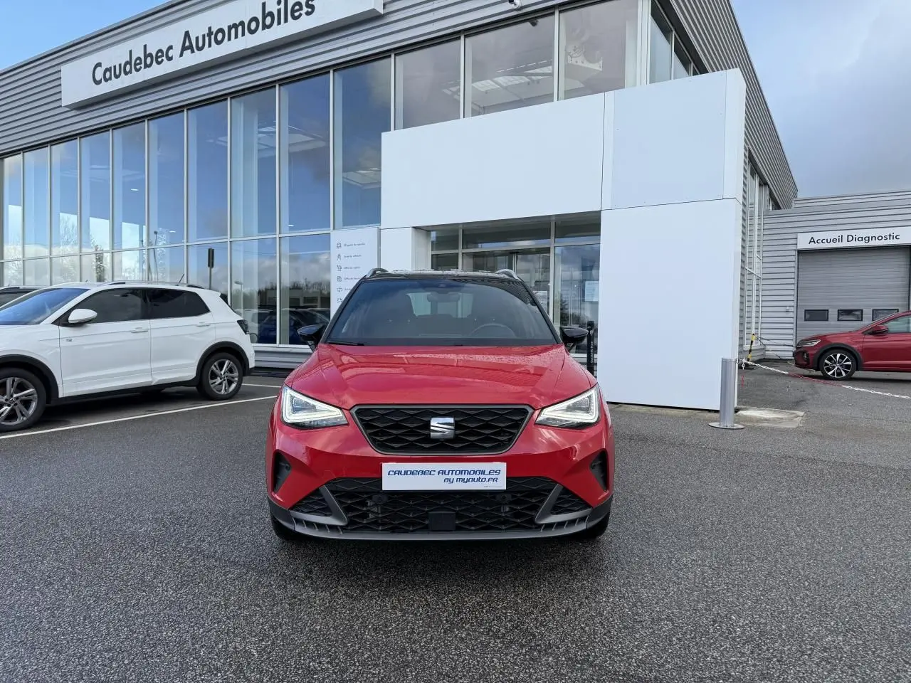 Vue frontale d’un SEAT Arona rouge avec calandre noire et projecteurs Full LED, stationné devant un concessionnaire.