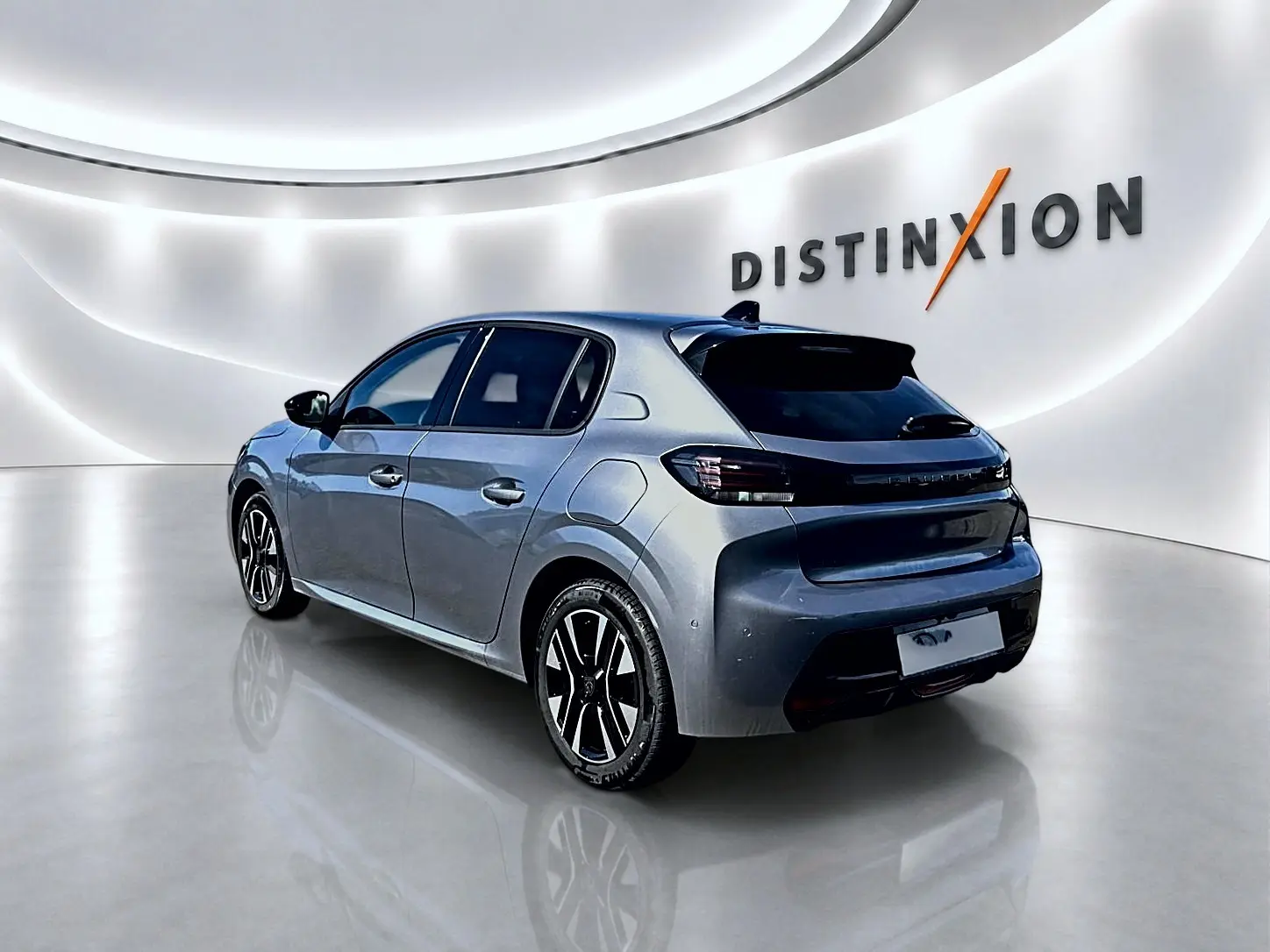Peugeot 208 gris artense vue 3/4 arrière droit, jantes alu noires et feux arrière à LED dans un showroom lumineux.