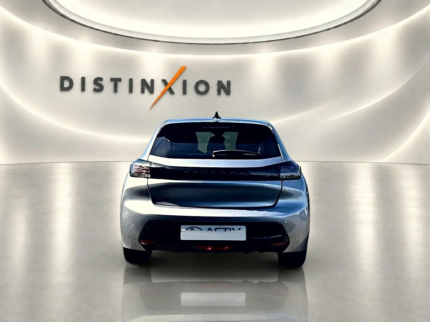 Vue arrière d'une Peugeot 208 1.2 100 Allure gris Artense dans un showroom avec éclairage doux et logo Distinxion en arrière-plan.