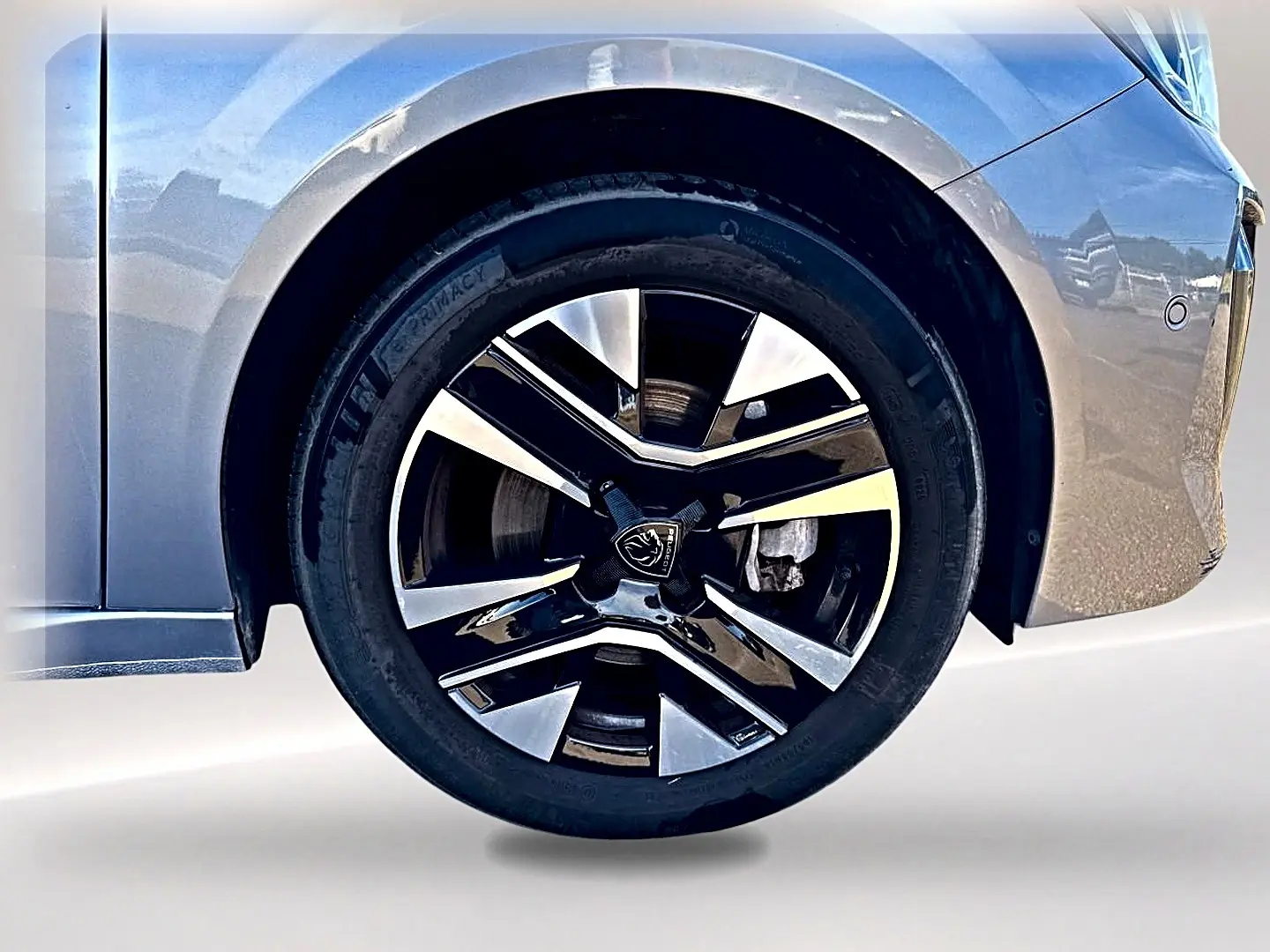 Gros plan sur la roue avant gauche de la Peugeot 208 1.2 100 Allure gris Artense avec jante alu bicolore.