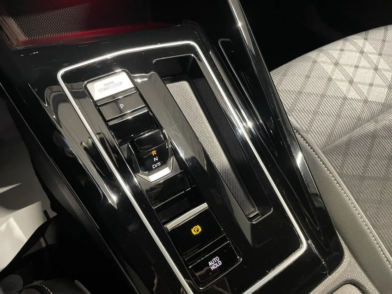 Gros plan sur la console centrale noire brillante avec levier de vitesses automatique et siège avant gris à motifs.