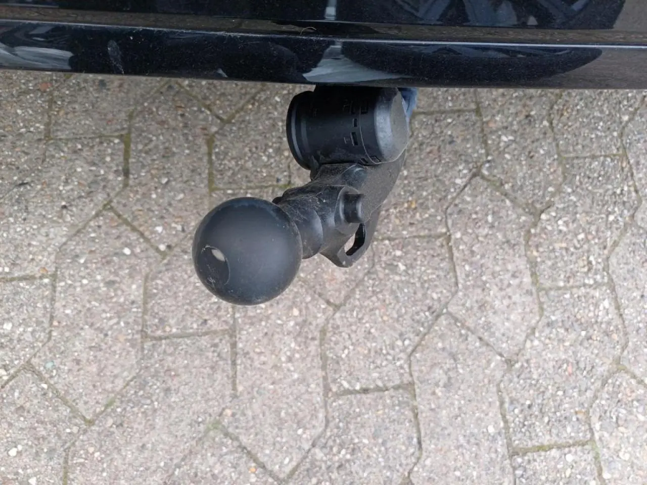Gros plan sur l'attelage escamotable noir sous le pare-chocs arrière d'une Volkswagen Golf blanche.