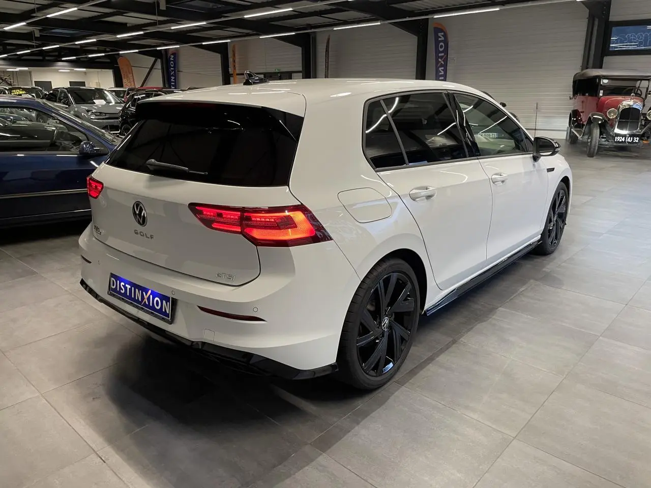 Vue 3/4 arrière droite d'une Volkswagen Golf 1.5 eTSI blanche avec jantes noires et vitres surteintées en intérieur showroom.