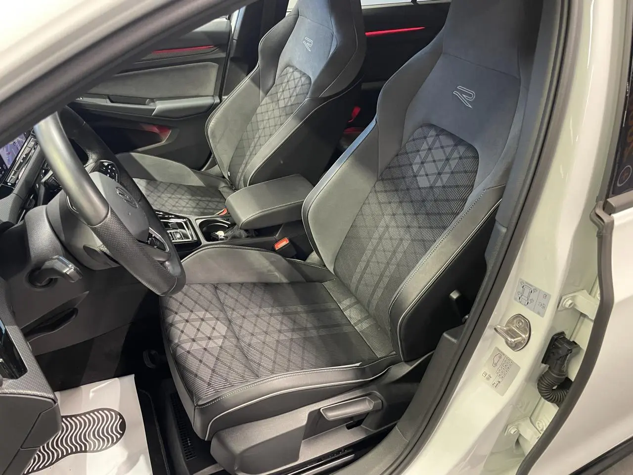 Vue intérieure côté conducteur de la Golf 8 R-Line blanche, sièges sport noirs avec surpiqûres et volant multifonctions.
