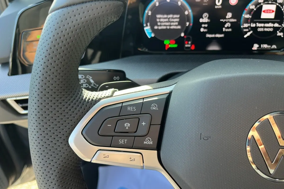 Gros plan sur le volant cuir perforé gris avec commandes multifonctions et tableau de bord numérique d'une Volkswagen Golf 2026.